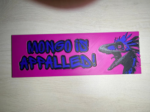 A rectangular pink sticker with a black and blue bird illustration and the text 'MONGO IS APPALLED!' in blue graffiti-style lettering, shown on a light wood surface.